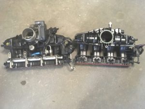 Old and new intake manifolds of a Volkswagen Tiguan side by side. Old intake manifold still has fuel line attached.
