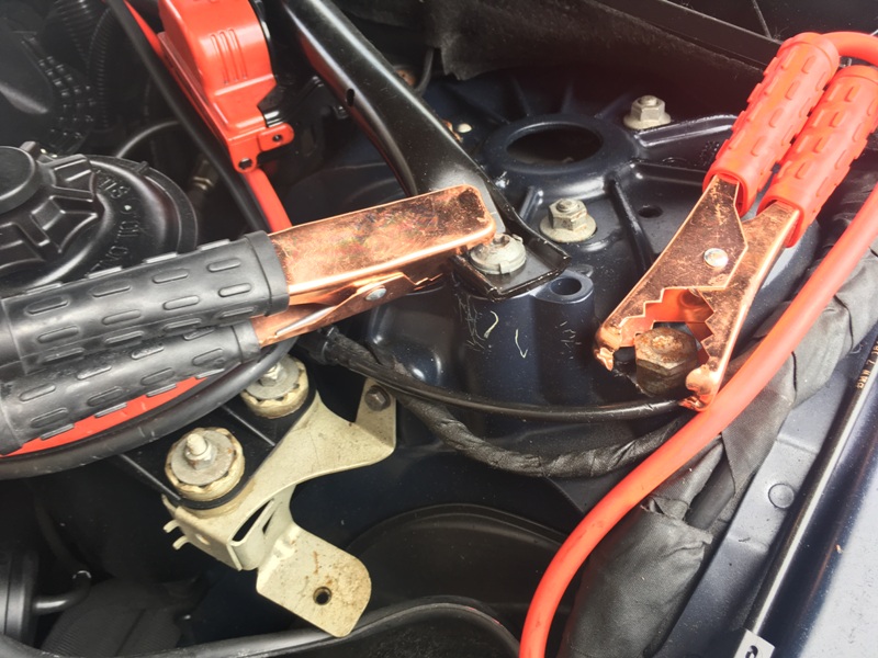 A set of Jump cables connected to strut mount grounding engine to body of vehicle.